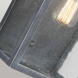 Close-up of the Hodges Outdoor Large Wall Lantern in Ash Black, showcasing its vintage-style charm. The clear seeded glass panels resemble rain-speckled surfaces, while the bulb casts a warm glow, crafting a rustic and cozy atmosphere reminiscent of prairie design.