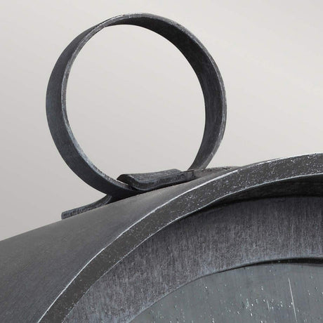 Close-up of the top of a vintage-style Hodges Outdoor Small Wall Lantern in ash black with a round handle. The surface is slightly weathered, giving it an antique look reminiscent of prairie design. The background is a neutral gray color.