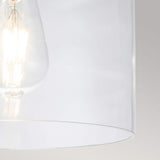 Close-up of a clear glass light bulb glowing warmly inside the Hounslow 1 Light Flush - Burnished Brass against a plain light gray background. The image highlights the bulb's filament and modern design, complemented by subtle burnished brass accents for an elegant touch.