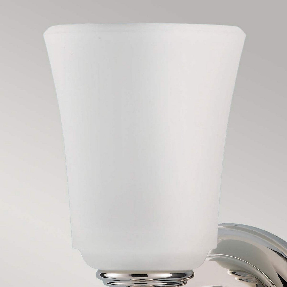 A close-up of the Huguenot Lake 1 Light Wall Light, featuring a frosted opal glass shade with a polished chrome base against a neutral background. The smooth, tapered shape of the glass imparts a modern and elegant appearance to this bathroom lighting fixture.