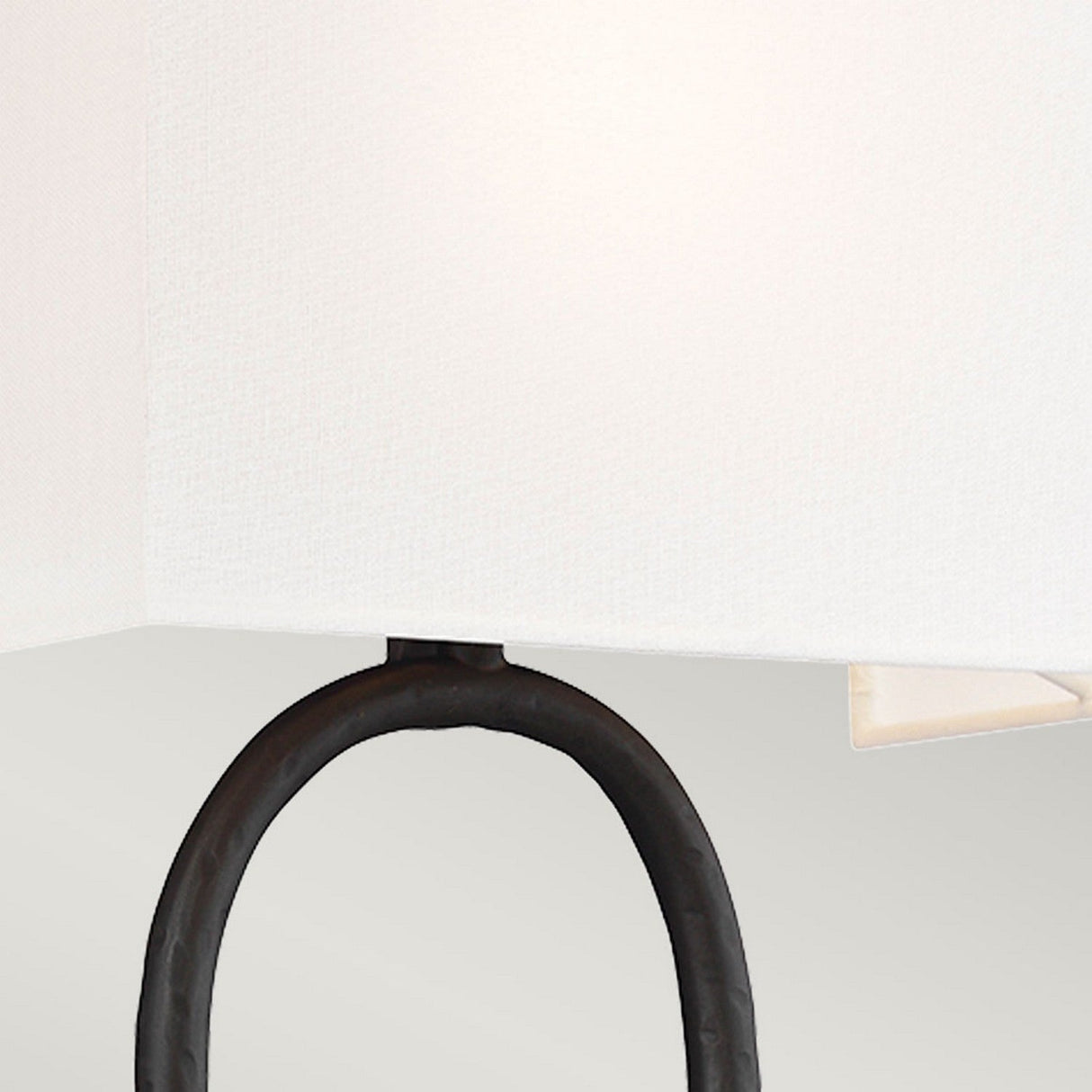 A detailed view of the Indo 1 Light Wall Light showcases its black, circular metal frame paired with an off-white cotton lampshade. The light's sleek, minimalist design and aged iron finish subtly contrast with the soft texture of the shade, delivering an elegant and modern aesthetic.