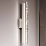 The Jessie 1 Light LED Wall Light, with its rectangular design and polished chrome finish, features a patterned side panel. The light softly illuminates a neutral-colored wall, crafting an elegant and contemporary ambiance.