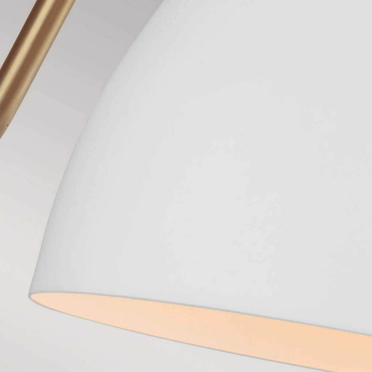 Close-up of the Joan 1 Light Wall Light in a modern, minimalist style. The lampshade features a smooth, matte white, cone-shaped design with a thin arm of burnished brass visible in the top left corner, all set against a light gray background.