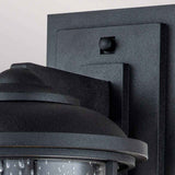 Close-up of the Lighthouse 1 Light Outdoor Medium Wall Lantern in textured black. This fixture showcases a simple, modern design with a clear glass enclosure featuring water-droplet texture, mounted on a flat rectangular backplate that subtly integrates nautical design elements.