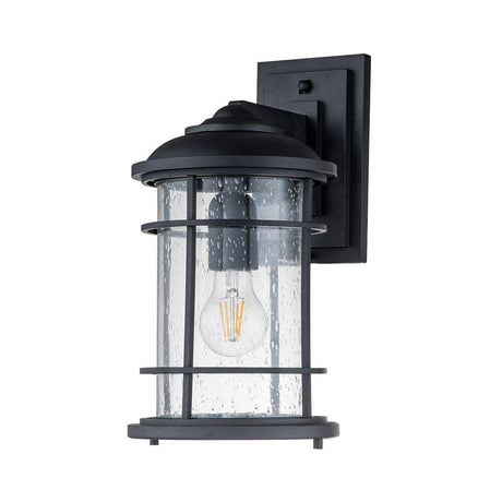 The Lighthouse 1 Light Outdoor Medium Wall Lantern in Textured Black showcases a speckled, clear cylindrical glass casing with a visible LED bulb. Its nautical design is beautifully complemented by a sleek rectangular black wall plate, enhancing the charm of any exterior space.