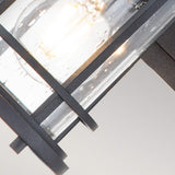 A close-up of the Lighthouse 1 Light Outdoor Small Wall Lantern in textured black metal, featuring clear glass panels. The illuminated bulb inside casts a warm glow that beautifully reflects and dances off the glass.