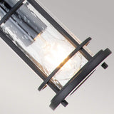 The Lighthouse 1 Light Outdoor Small Chain Lantern in Textured Black features a lit bulb inside a cylindrical fixture covered with clear seeded glass, giving it a bubbled look. This is enhanced by the frame's matte black metal finish, while the soft gray gradient background adds to its elegant nautical lantern appearance.