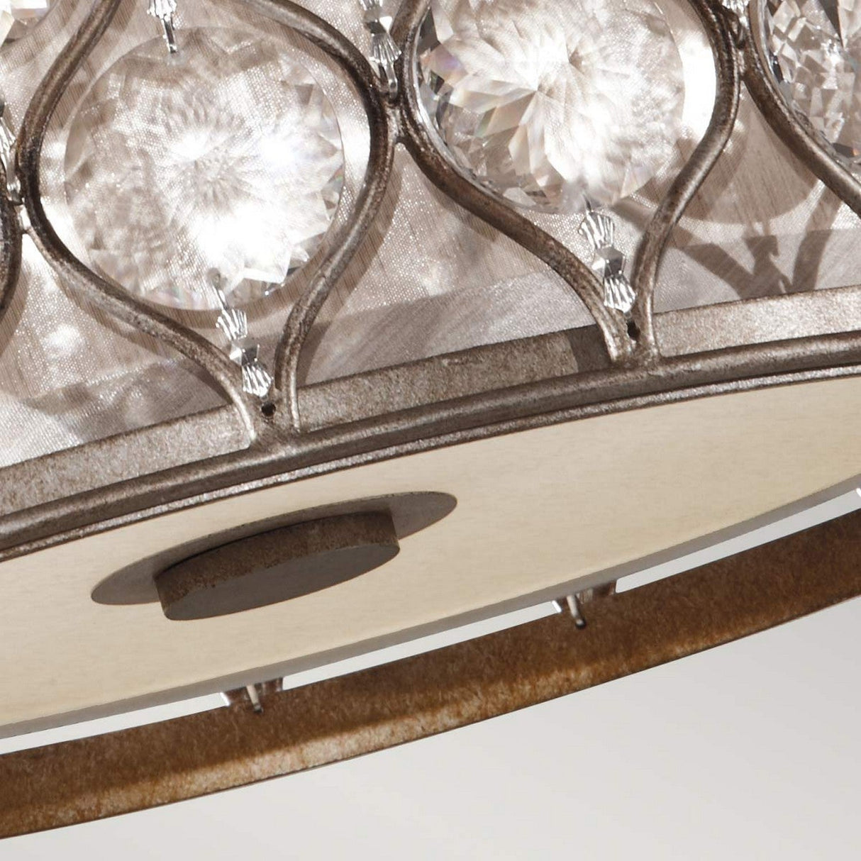An intricate close-up highlights the Lucia 2 Light Flush chandelier, boasting an ornate circular frame adorned with Bauhinia crystals. The patterned grid design of the crystals creates dazzling light reflections, while a soft neutral backdrop accentuates its sophisticated burnished silver finish.