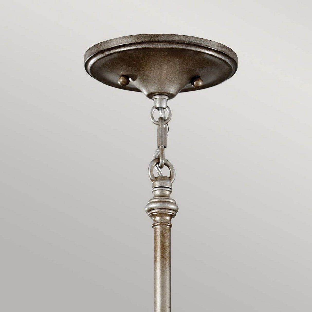 The Lucia 6 Light Chandelier in burnished silver showcases a close-up of its ceiling mount, featuring a round canopy and hanging rod linked by chain links. Its elegant hardware is set against a light gray background, imparting a vintage aesthetic.