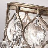 The Lucia 1 Light Wall Light in Burnished Silver showcases an antique finish with large Bauhinia crystals. These faceted pendants capture and reflect light, creating intricate patterns on the surrounding fabric. The metal features a burnished silver touch, elevating its elegant design.