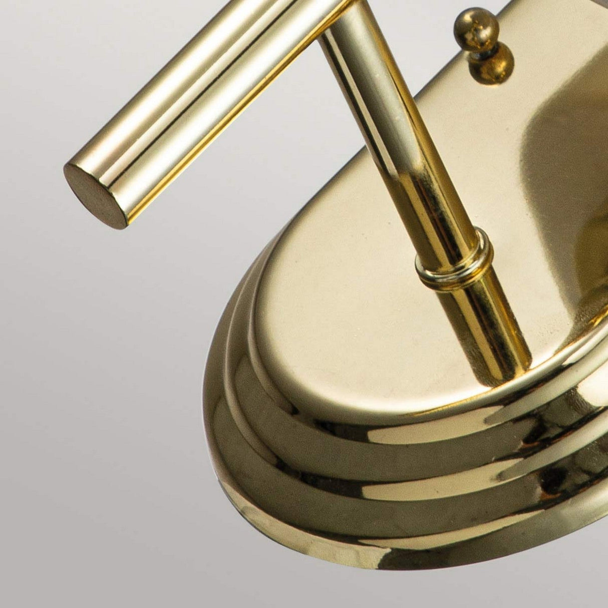 A close-up of the polished brass Malibu 1 Light Wall Light showcases its modern design, complete with a cylindrical element attached to an oval base. The surface reflects light beautifully, highlighting its gleaming finish.