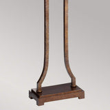 Close-up of the Marcella 1 Light Floor Lamp in bronze, showcasing its metal stand with a square base and two vertical, curved supports. The rustic, weathered finish on the metal adds vintage glamour against a plain, light gray background.