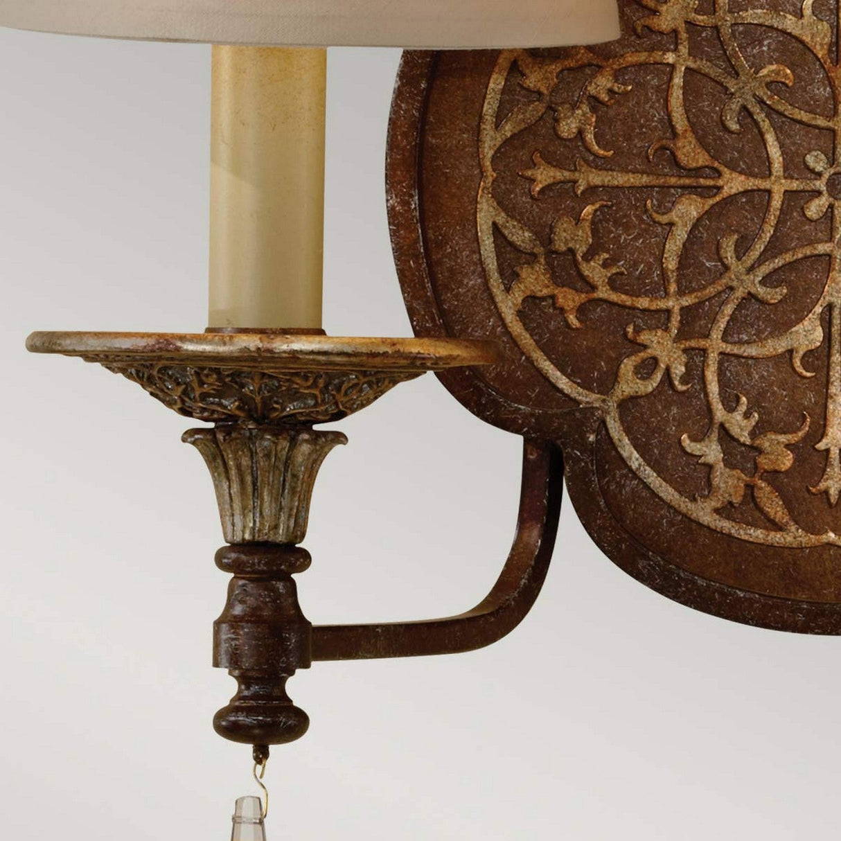 Detailed view of the Marcella 2 Light Wall Light in bronze, showcasing its vintage-style design with a decorative iron backplate embellished with intricate filigree detailing. The sconce features a candle-like structure supporting two lights, lending an antique touch against a soft gray background, ideal for luxury home decor.