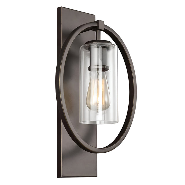 The Marlena 1 Light Wall Light in antique bronze features a modern design with a cylindrical glass shade and an exposed bulb. It's framed by a circular metal frame and mounted on a rectangular backplate, offering a touch of geometric elegance.