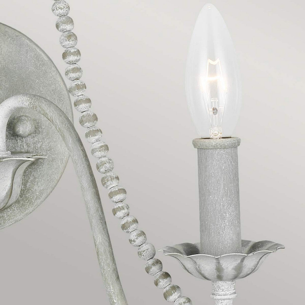 Close-up of the Maryville 2 Light Wall Light in a washed grey finish, featuring candle-shaped bulbs that exude rustic charm. The fixture boasts a textured, metallic appearance with decorative bead detailing and a flower-petal base for the bulbs, creating a French country feel against a plain background.