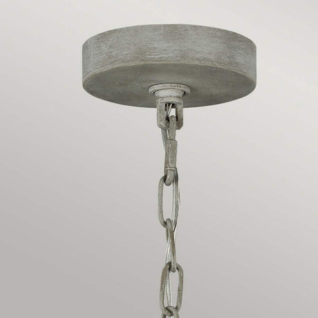 A close-up of a ceiling light fixture with a metallic, circular canopy and a chain hanging from it exudes rustic charm. This Maryville 9 Light Chandelier - Washed Grey stands out against a plain, light gray background, effortlessly blending elegance with French Country sophistication.