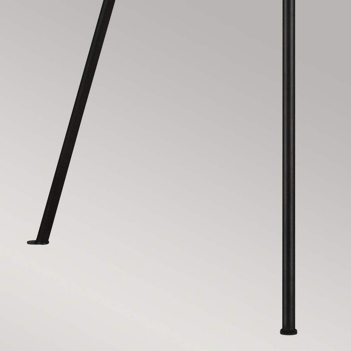 Close-up of the black metal legs of a tripod against a plain grey background, highlighting their sleek and minimalist design reminiscent of the Penny 1 Light Floor Lamp in Iron/White.