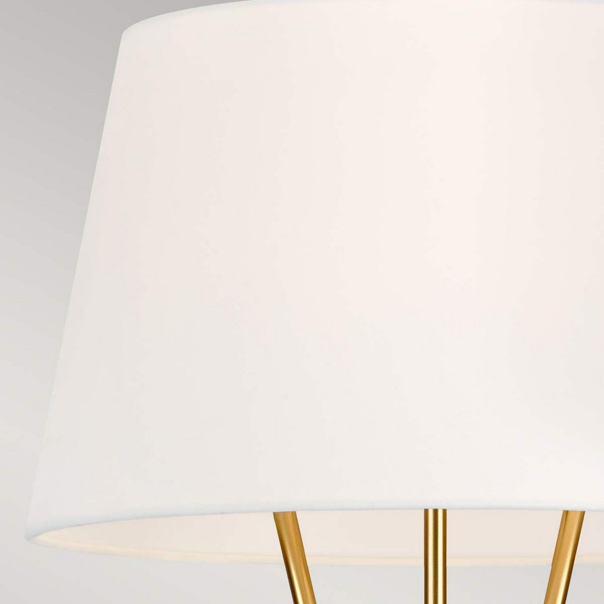 A close-up shot of the Penny 1 Light Floor Lamp - Burnished Brass displays its modern design, featuring a white lampshade and burnished brass legs. The light gray background enhances its mid-century elegance and minimalist sophistication.