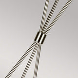 A close-up of the Penny 1 Light Floor Lamp in polished nickel highlights intersecting metal rods with a cylindrical connector at the center, all set against a simple background. This modern design showcases a symmetrical, geometric pattern that evokes sophistication.