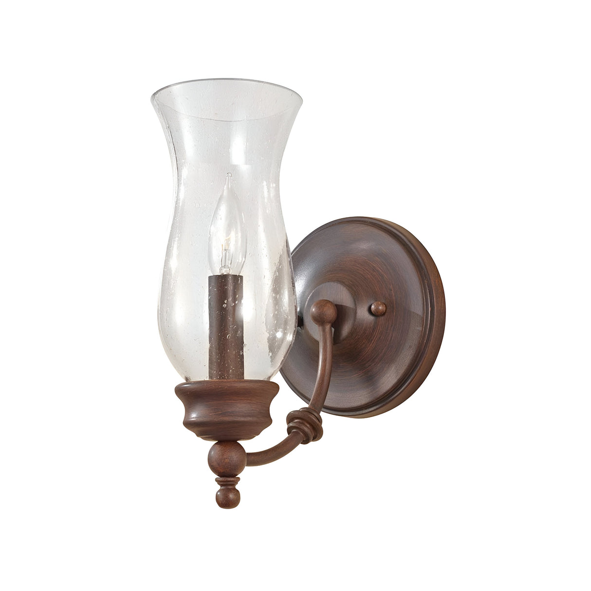 The Pickering Lane 1 Light Wall Light - Bronze features a farmhouse décor-inspired design with a curved arm and traditional elegance. It includes a clear glass shade reminiscent of a storm glass lantern, housing a single candle-shaped bulb, and is completed with a round backplate in Heritage Bronze.