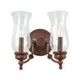 The Pickering Lane 2 Light Wall Light - Bronze is a vintage-style wall sconce with a traditional aesthetic. It features two glass hurricane shades and candle-shaped bulbs. This fixture, finished in Heritage Bronze, showcases curved arms and decorative finials reminiscent of storm glass lanterns, all attached to a circular backplate.