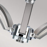 A close-up of the Prospect Park 5 Light Chandelier - Satin Nickel With Chrome highlights its modern elegance with sleek, curved arms and a polished finish. The central fixture and intersecting elements enhance its contemporary charm, making it ideal for transitional spaces against a light gray background.