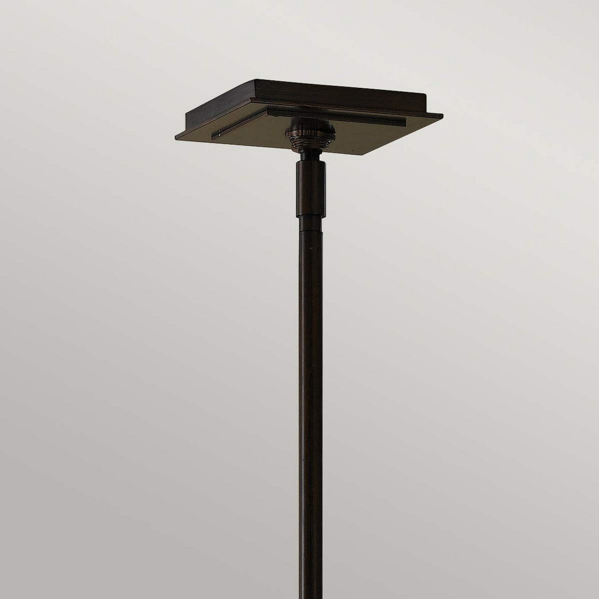 The Remy 1 Light Pendant Light showcases a minimalist design, featuring a sleek and slender stand complemented by a square, flat top in an elegant Heritage Bronze finish against a simple gray backdrop. The style is both contemporary and timeless.