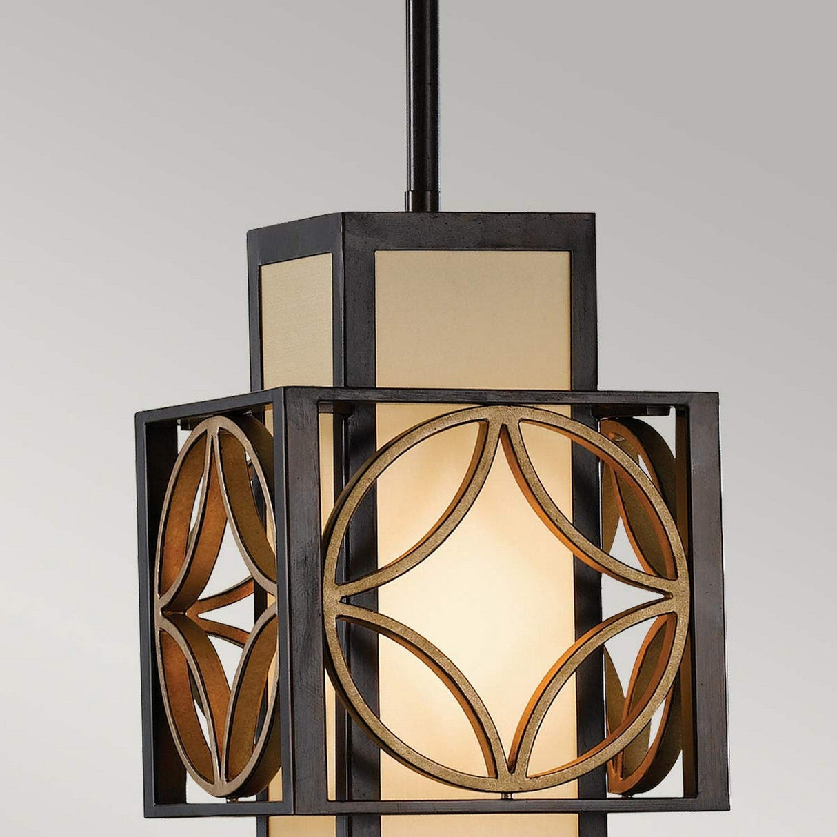 The Remy 1 Light Pendant Light in Heritage Bronze/Parissiene Gold features a contemporary design with a geometric metal frame that encases a frosted glass shade. It boasts circular patterns, a dark finish, and is suspended by a black rod, casting a warm glow when illuminated.