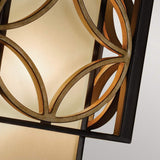 Close-up of the Remy 1 Light Wall Light, a decorative sconce featuring intersecting circular metal patterns in a Heritage Bronze and Parisienne Gold finish. The frosted glass background diffuses warm light, while geometric shapes contribute to its modern aesthetic inspired by French Arts and Crafts elegance.