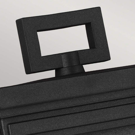 A close-up of the Roscoe 1 Light Outdoor Medium Wall Lantern in black, showcasing its matte finish and handle with an open rectangular grip, set against a light gray background. The lantern features ridged details on one side for a textured appearance.