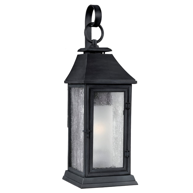 Introducing the Shepherd 2 Light Outdoor Medium Wall Lantern in Dark Weathered Zinc: a black metal fixture that showcases a classic Parisian design. It features clear glass panels and a loop handle on top, while its subtly tapered roof adds an elegant flair. The weather-resistant construction guarantees enduring beauty.