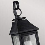 Close-up of the Shepherd 1 Light Outdoor Small Wall Lantern in Dark Weathered Zinc, ideal for vintage outdoor lighting. It features an angled design with a triangular top and loop handle. This weather-resistant lantern includes four glass panes and has a slightly weathered texture, set against a plain light gray background.