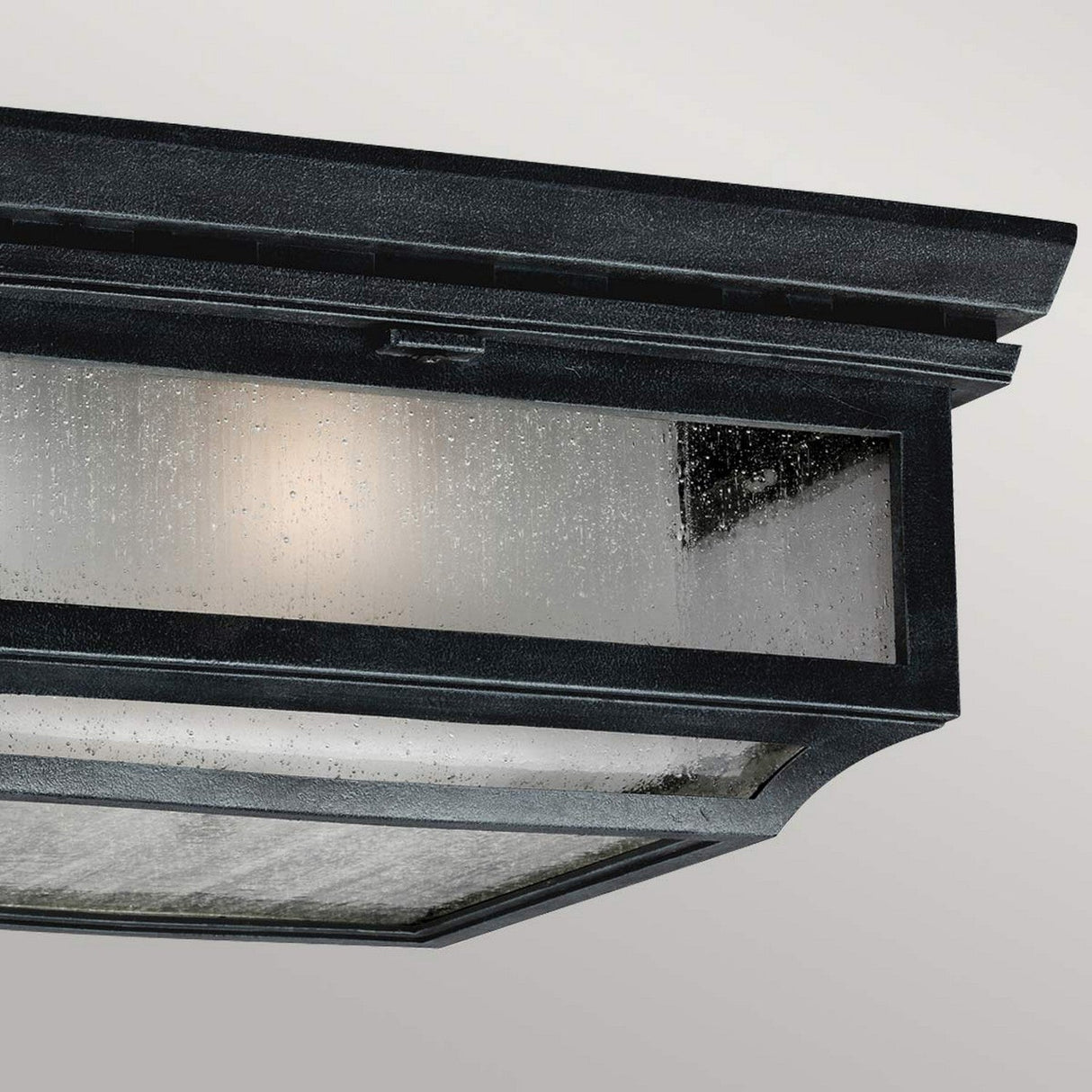 Close-up of the Shepherd 2 Light Outdoor Flush in Dark Weathered Zinc, showcasing its rectangular, weather-resistant metal structure with glass panels that emit a soft glow. This vintage-style lantern features a textured surface and is suspended against a plain gray background.