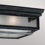 Close-up of the Shepherd 2 Light Outdoor Flush in Dark Weathered Zinc, showcasing its rectangular, weather-resistant metal structure with glass panels that emit a soft glow. This vintage-style lantern features a textured surface and is suspended against a plain gray background.