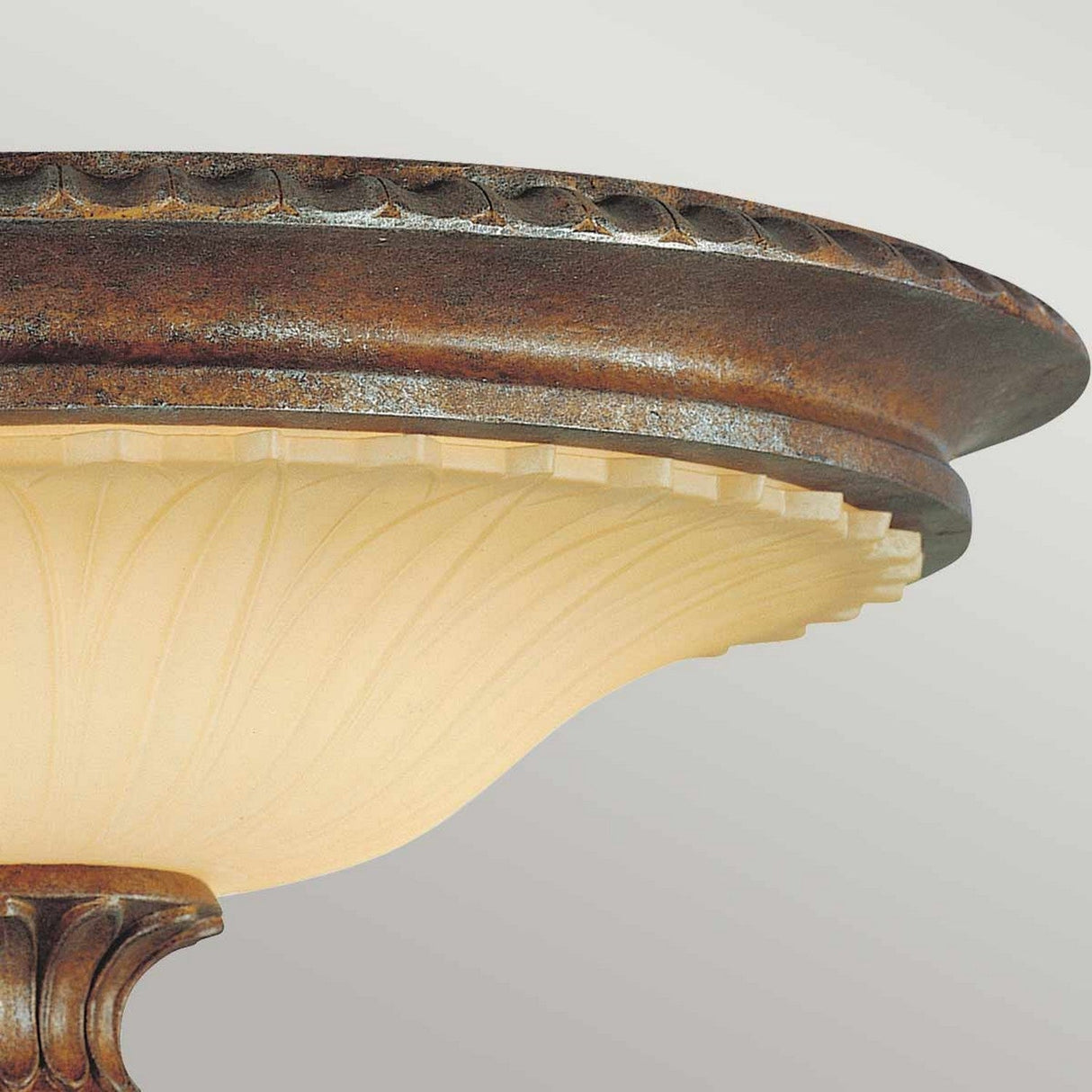 Close-up of the Stirling Castle 2 Light Flush in bronze. This fixture features a textured bronze-colored edge with a patterned rim and a frosted glass bowl. The design is elegant and traditional, casting a warm glow beneath, reminiscent of a Gothic arch design.