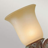 A close-up of a lit, frosted glass lamp shade emitting a soft, warm glow with vintage appeal. The Stirling-1 Castle 1 Light Wall Light - Bronze is mounted on a metal fixture with an ornate base. The background features a plain, light gray color.