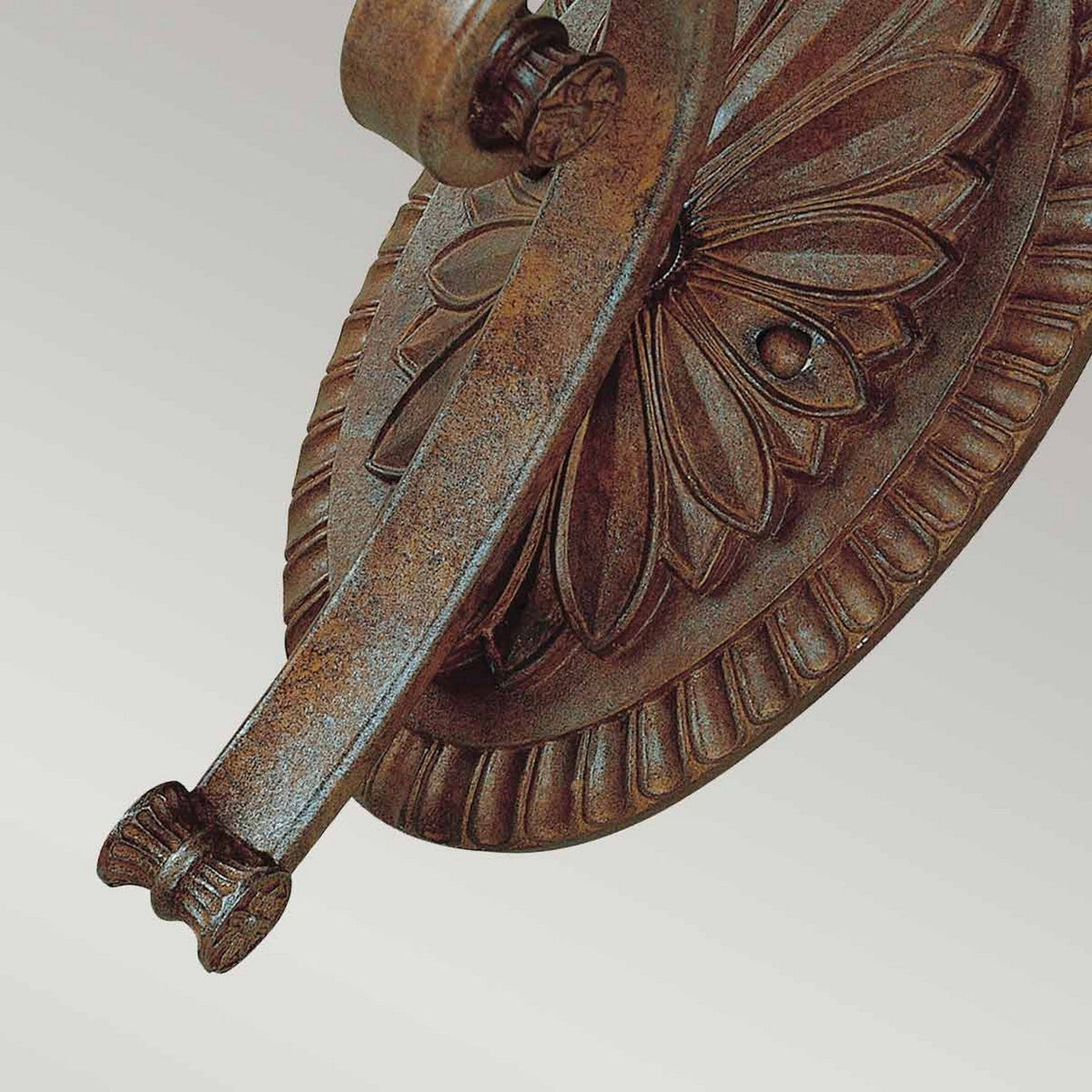 Close-up of an intricately designed, weathered bronze wall fixture with floral and ridged patterns exuding vintage appeal. The arm gracefully extends from a circular base, reminiscent of the Stirling-1 Castle 1 Light Wall Light - Bronze, highlighting its antique-look craftsmanship against a soft gray background.