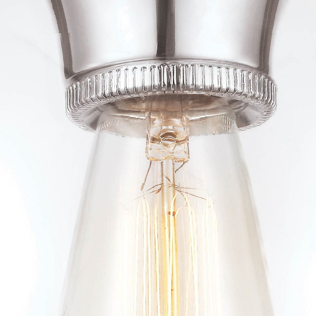 A detailed view of the Tabby 1 Light Flush - Polished Nickel reveals a vintage-style bulb set in its sleek nickel socket. The bulb casts a gentle, warm light that accentuates the filaments' detailed design and the metal's textured surface, capturing modern illumination with an enduring elegance.