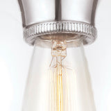 A detailed view of the Tabby 1 Light Flush - Polished Nickel reveals a vintage-style bulb set in its sleek nickel socket. The bulb casts a gentle, warm light that accentuates the filaments' detailed design and the metal's textured surface, capturing modern illumination with an enduring elegance.
