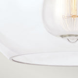 Close-up of the Tabby 1 Light Flush - Polished Nickel. Its modern glass construction highlights a detailed filament within a clear, sleek shade. This contemporary lighting fixture emits a gentle light, creating a cozy atmosphere.