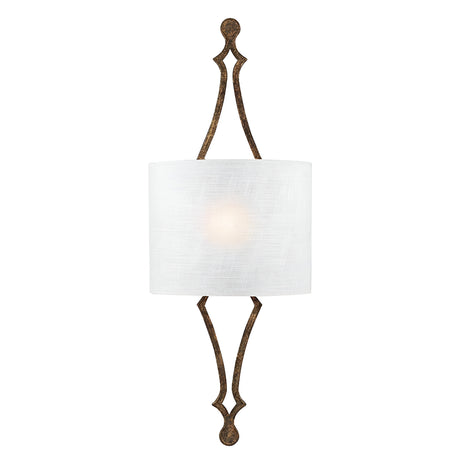 The Tilling 1 Light Wall Light in Antique Gold features a traditional design with an elongated, decorative metal frame and a dark finish. It is adorned with a cylindrical white linen shade that emits a soft glow at its center, offering an elegant and symmetrical aesthetic.