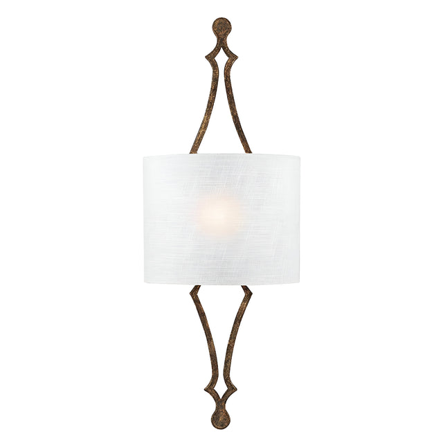 The Tilling 1 Light Wall Light in Antique Gold features a traditional design with an elongated, decorative metal frame and a dark finish. It is adorned with a cylindrical white linen shade that emits a soft glow at its center, offering an elegant and symmetrical aesthetic.