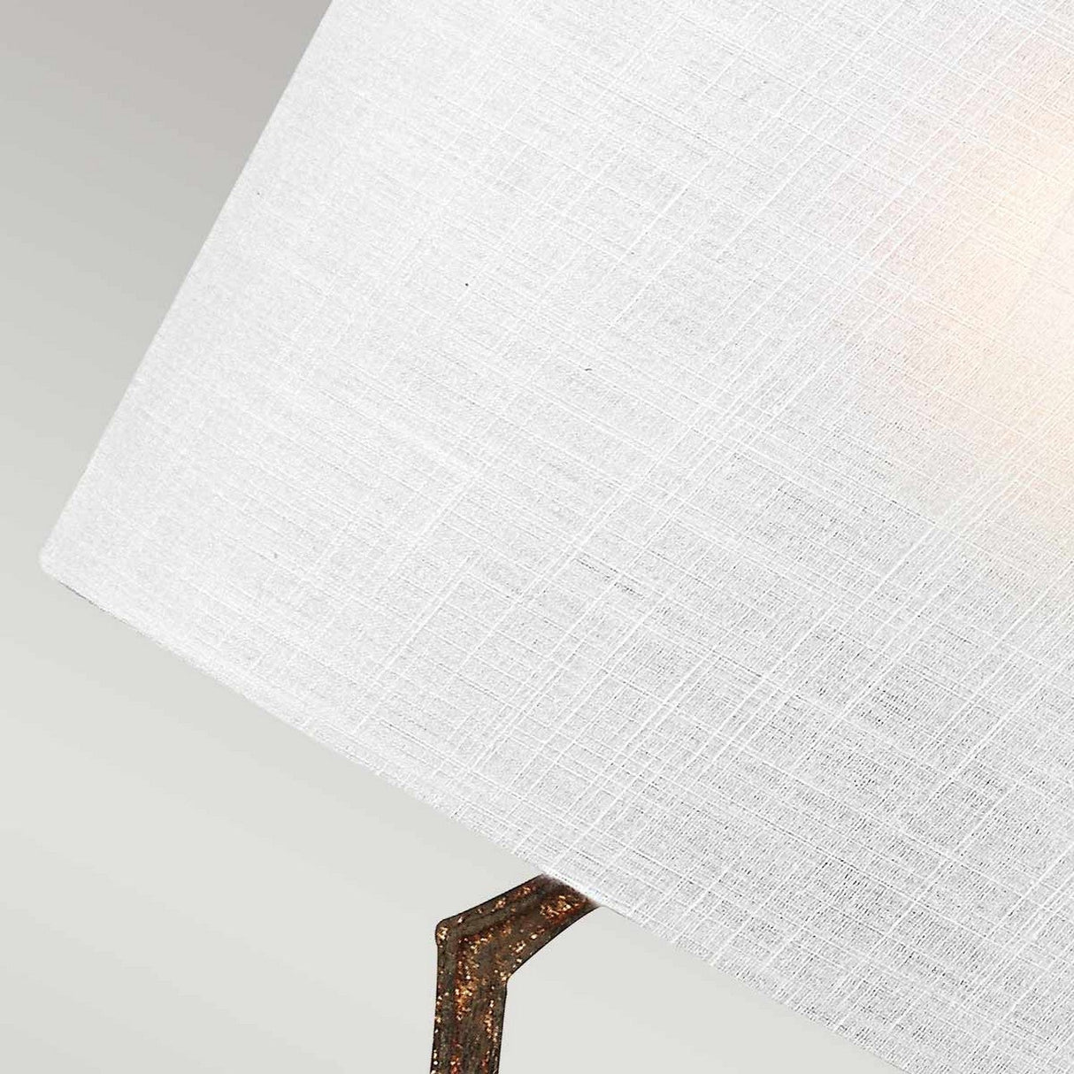 Close-up of the Tilling 1 Light Wall Light in Antique Gold, showcasing a white linen shade and a partially visible metal lamp arm. The texture of the fabric is prominent, with soft lighting casting a golden glow.