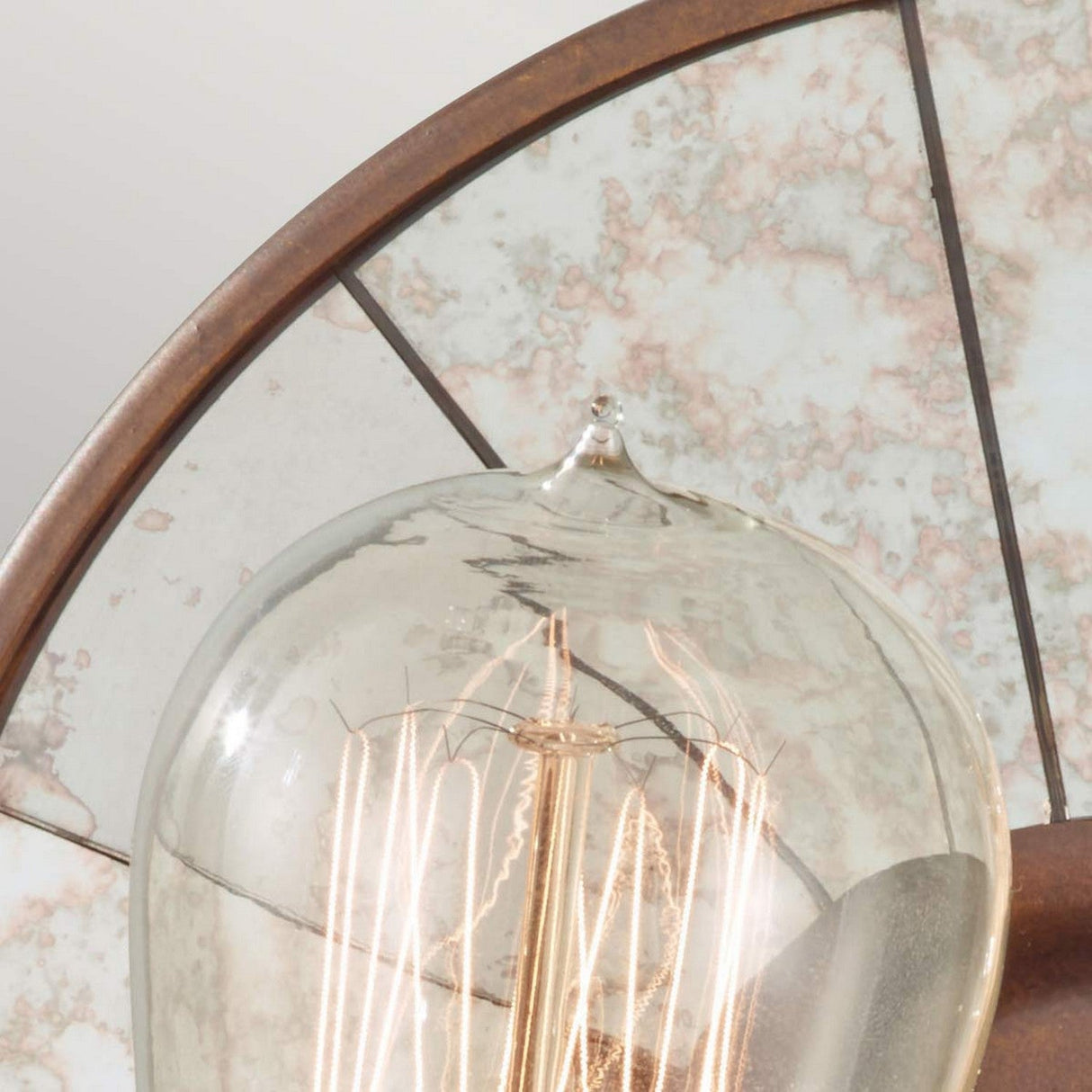 Close-up of an Urban Renewal 1 Light Wall Light - Bronze with exposed filament inside a glass casing. The bulb is mounted on a fixture with a circular bronze-colored support, perfect for adding vintage lighting charm against a rustic, marbled backdrop.