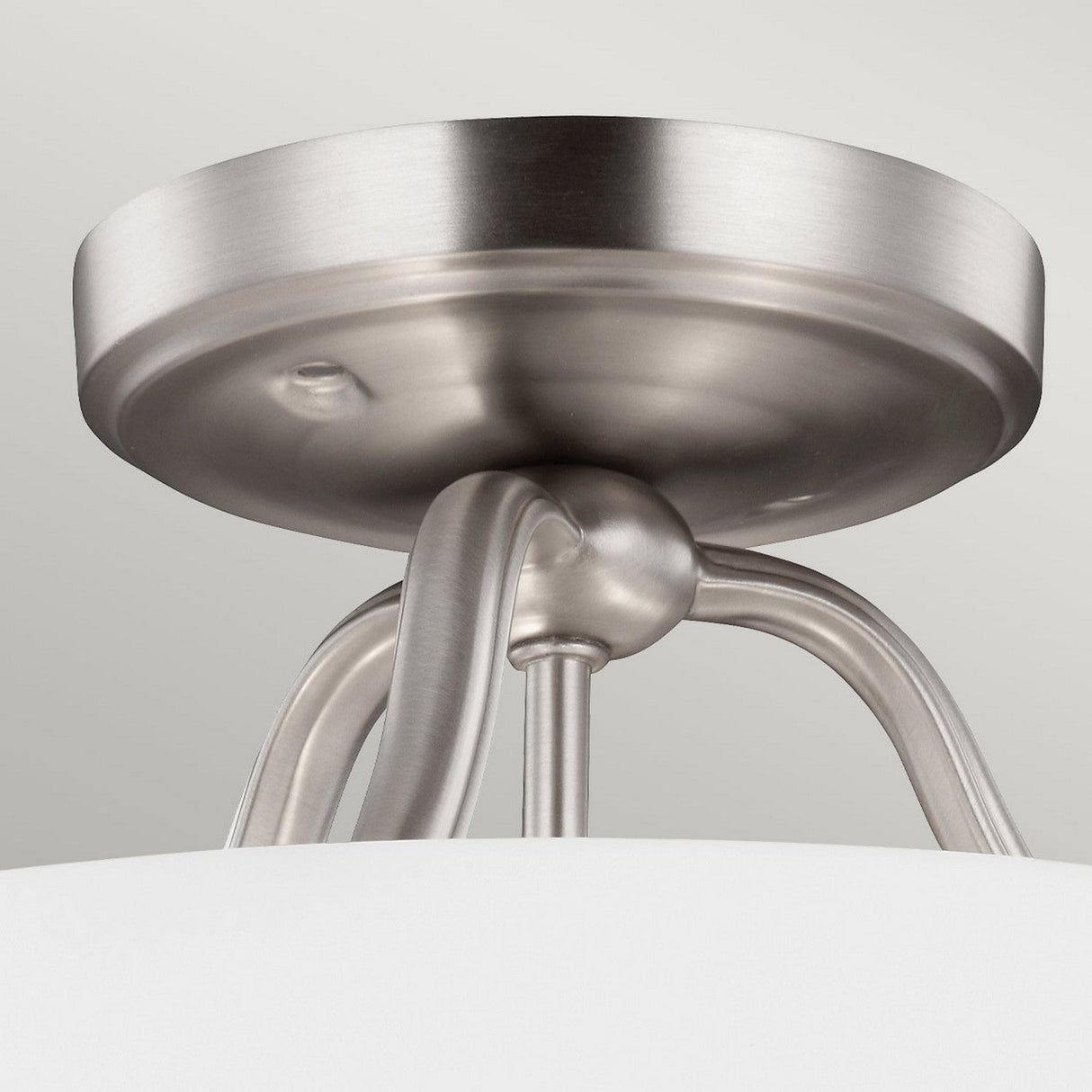 A close-up of the Vintner 3 Light Semi Flush in satin nickel showcases a modern ceiling light fixture with a sleek, circular base and elegantly curved supports that perfectly complement its white lampshade.