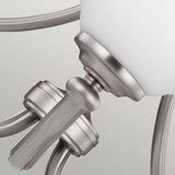 Close-up of a brushed satin nickel wall sconce fixture showcasing an opal etched glass shade. The gracefully curved arm and connecting joint emphasize its sleek modern design, standing elegantly against a neutral background, reminiscent of the Vintner 3 Light Chandelier in Satin Nickel.