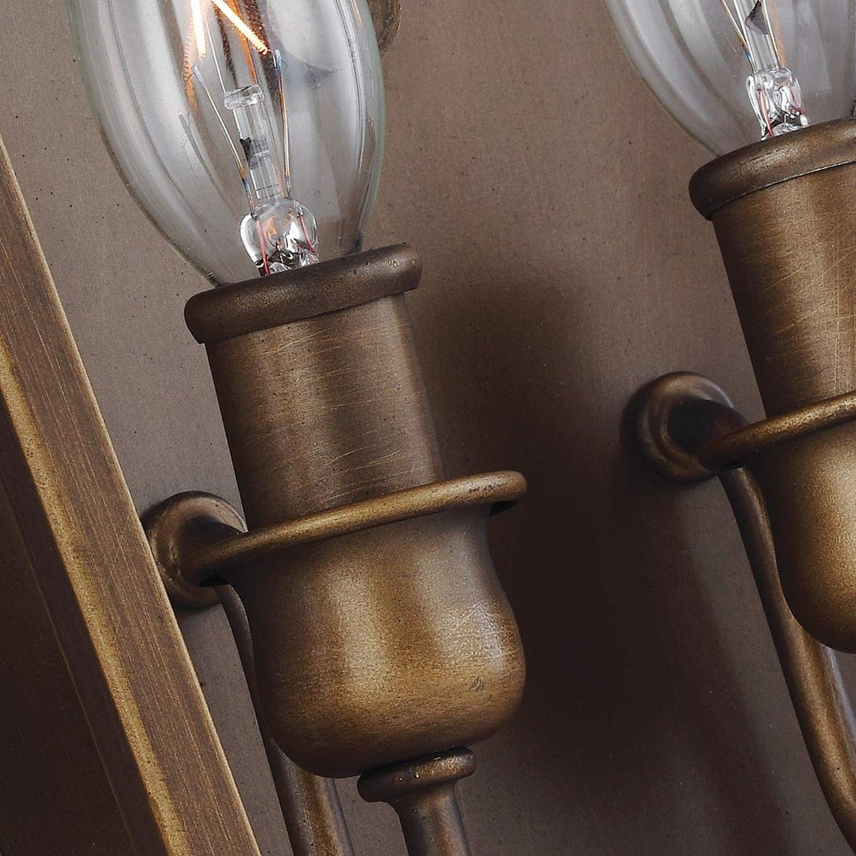 A close-up of two Yarmouth 2 Light Wall Lights, featuring exposed filament bulbs and mounted on a textured beige wall. These fixtures showcase a classic curved design with a painted aged brass finish that exudes a warm metallic glow, embodying a minimalist aesthetic.