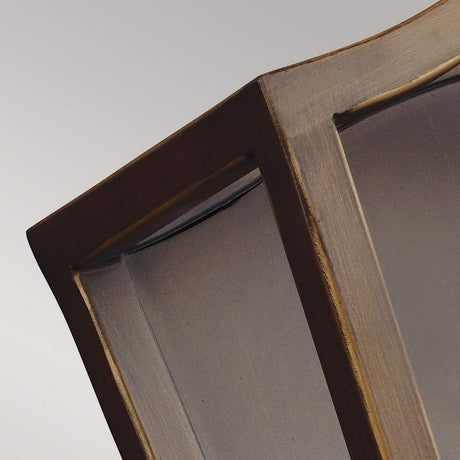 Close-up of a corner of a wooden window frame with curved glass panes against a light gray background. The window frame, reminiscent of traditional lanterns, boasts a smooth finish and a warm, natural wood color similar to the painted aged brass seen in the Yarmouth 3 Light Wall Light.