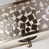 A close-up of the Zara 3 Light Semi Flush- Brushed Steel showcases a mosaic of metal squares and rectangles, perfectly capturing a contemporary geometric design. This stylish fixture is set against a frosted glass background, contributing to its elegant, modern appeal.