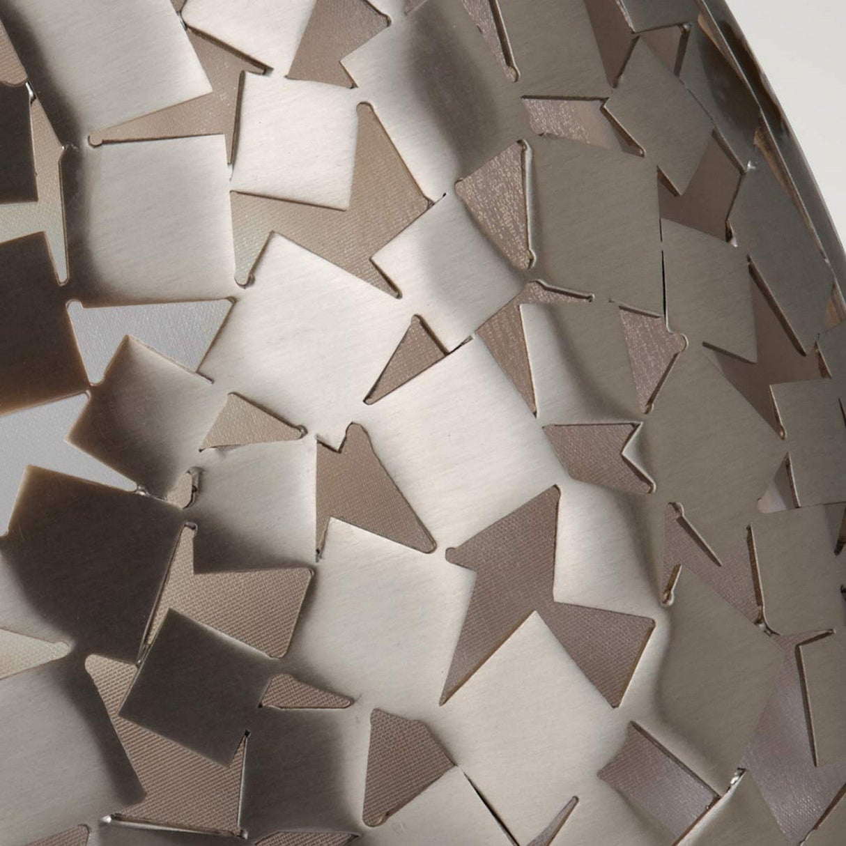 Close-up of a metallic surface with an abstract pattern of interlocking, triangular shapes in varying shades of silver and bronze, reminiscent of contemporary design. This textured, reflective appearance evokes the sleek elegance similar to the brushed steel elements found in the Zara 1 Light Wall Light - Brushed Steel.